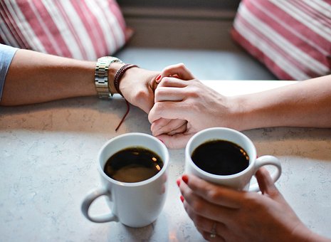 Zwei Personen die Hände halten und Kaffee trinken