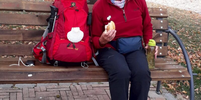 Frau sitzt auf Bank, neben ihr ein Rucksack