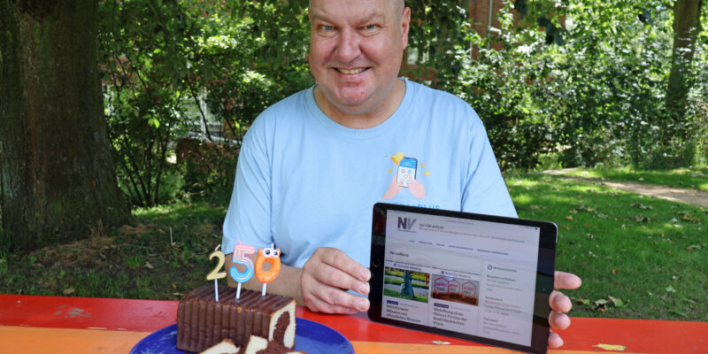 Ein Mann mit einem Tablet in der Hand sitzt auf einer Bank, auf der ein Kuchen steht.