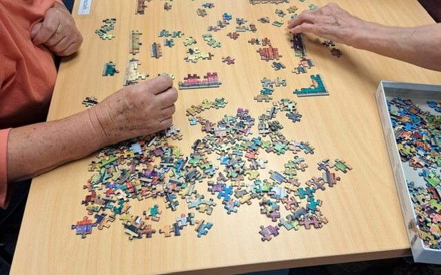 Tisch mit Puzzle-Teilen und Händen, die puzzeln