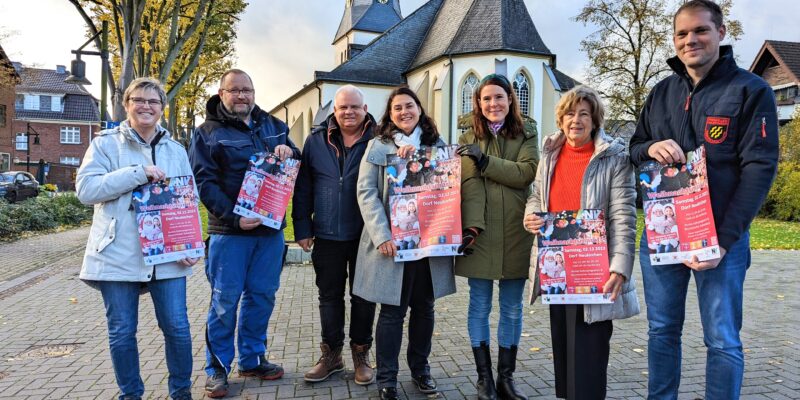 Vier Frauen und drei Männer stehen nebeneinander und halten Plakate. Im Hintergrund ist eine Kirche